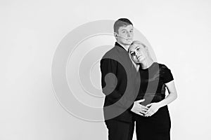 Pregnant woman and her husband hugging and holding onto your stomach in black clothes on a white background. Black and white