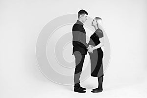 Pregnant woman and her husband hugging and holding onto your stomach in black clothes on a white background. Black and white