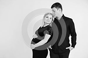 Pregnant woman and her husband hugging and holding onto your stomach in black clothes on a white background. Black and white