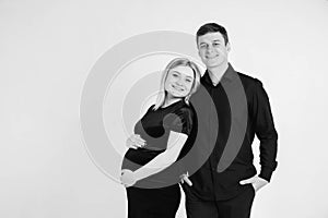 Pregnant woman and her husband hugging and holding onto your stomach in black clothes on a white background. Black and white