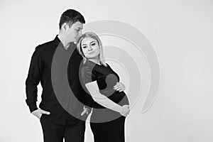 Pregnant woman and her husband hugging and holding onto your stomach in black clothes on a white background. Black and white