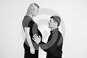 Pregnant woman and her husband hugs the belly of a pregnant wife in black clothes on a white background. Black and white picture.