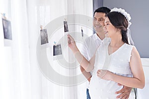 Pregnant woman and her husband looking ultrasound scan photo on the window