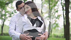 A pregnant woman with her husband rests in the park in nature. Caring for a pregnant wife.