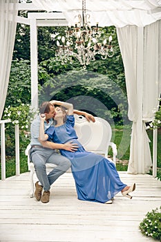 Pregnant woman and her husband sitting and hugging at cozy cafe terrace in the fall.