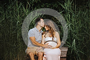 Pregnant woman and her husband sitting at a lake while he is kissing her forehead gently