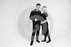 Pregnant woman and her husband smiling in black clothes on a white background. Black and white picture. Beautiful married couple.