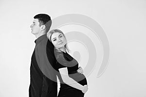 Pregnant woman and her husband smiling in black clothes on a white background. Black and white picture. Beautiful married couple.