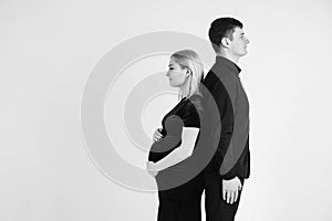 Pregnant woman and her husband stand with your back to each other in black clothes on a white background. Black and white picture