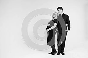 Pregnant woman and her husband stand with your back to each other in black clothes on a white background. Black and white picture