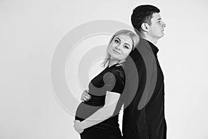 Pregnant woman and her husband stand with your back to each other in black clothes on a white background. Black and white picture