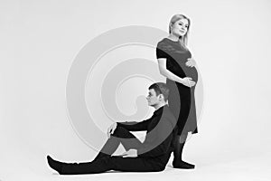 Pregnant woman and her husband stand with your back to each other in black clothes on a white background. Black and white picture