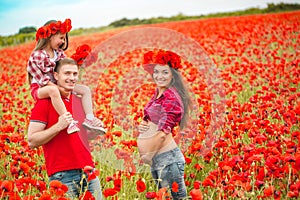 Pregnant woman her husband and their daughter in poppy field