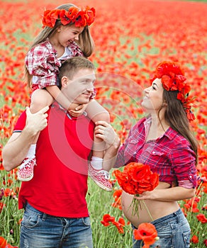 Pregnant woman her husband and their daughter in poppy field