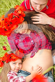Pregnant woman her husband and their daughter in poppy field