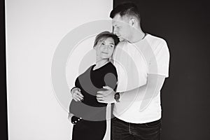 Pregnant woman with her lovely husband hug each other and put hand on belly. Studio photosession. Black and white