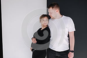 Pregnant woman with her lovely husband hug each other and put hand on belly. Studio photosession. Black and white