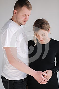 Pregnant woman with her lovely husband hug each other and put hand on belly. Studio photosession. White background