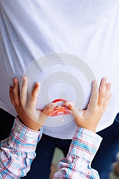 Pregnant woman and her young daughter`s hands holding baby`s dum