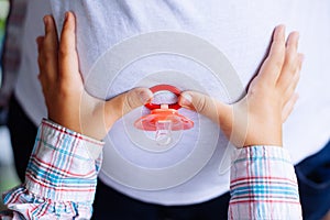 Pregnant woman and her young daughter`s hands holding baby`s dum