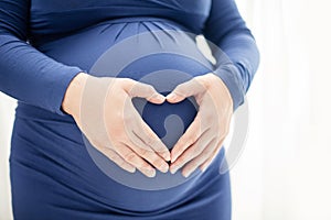 Pregnant woman hold heart-shaped hands on her baby bump
