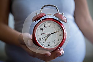 Pregnant woman holding an alarm clock showing impending birth