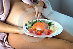 Pregnant attractive woman with soft skin and beautiful belly having a breakfast in bed, she is holding her belly in 2nd trimester photo
