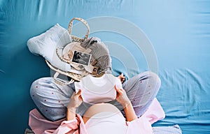 Pregnant woman holding baby bodysuit preparing to child birth during pregnancy. Mother with wicker basket with stuff for baby and