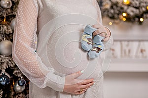 Pregnant woman holding baby booties. Belly with booties close up