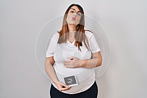 Pregnant woman holding baby ecography looking at the camera blowing a kiss being lovely and sexy