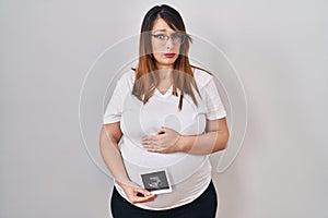 Pregnant woman holding baby ecography skeptic and nervous, frowning upset because of problem