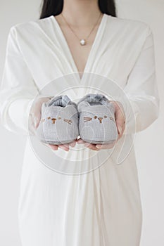 Pregnant woman holding baby shoes in hand