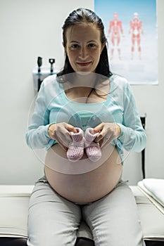 Pregnant woman holding baby shoes in hospital