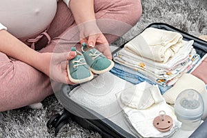 Pregnant woman holding baby shoes and packing maternity hospital bag. Mother during pregnancy waiting for baby preparing