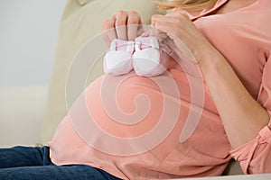Pregnant Woman Holding Baby Shoes On Sofa