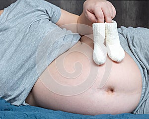 Pregnant woman holding baby small shoes in hands. Maternity prenatal care and woman pregnancy concept