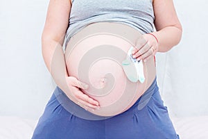 Pregnant woman holding baby socks near the belly.