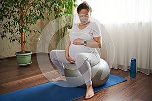 Pregnant woman holding belly, sitting barefoot on a fit ball and mat, doing breathing exercises for easy childbirth.