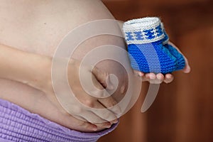 Pregnant woman holding blue baby booties on belly, closeup