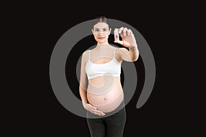Pregnant woman holding a bottle of pills against her belly at colorful background with copy space. Taking medication during
