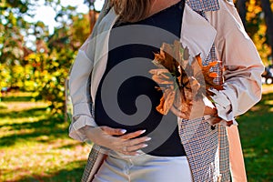 A pregnant woman holding a bouquet of yellow leaves in the autumn forest.