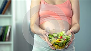 Pregnant woman holding bowl of vegetable salad rich in vitamins and nutrients