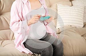 Pregnant woman holding box with pills at home, closeup