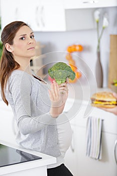 pregnant woman holding broccoli and refusing burger