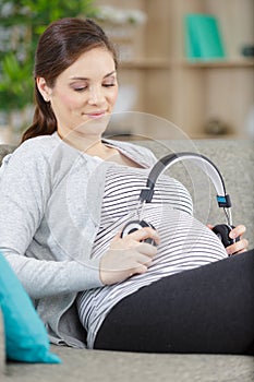 pregnant woman holding earphones near belly
