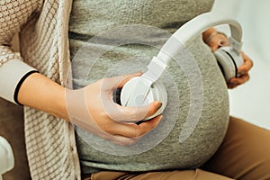 Pregnant woman holding earphones near her belly