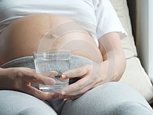 Pregnant woman holding glass of water relaxing at home.