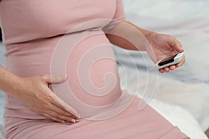 Pregnant woman holding glucose meter and checking blood sugar level by herself at home. gestational diabetes concept