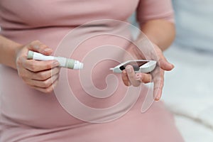 Pregnant woman holding glucose meter and checking blood sugar level by herself at home. gestational diabetes concept