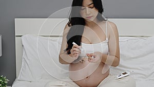 Pregnant woman holding glucose meter and checking blood sugar level by herself at home. gestational diabetes concept.